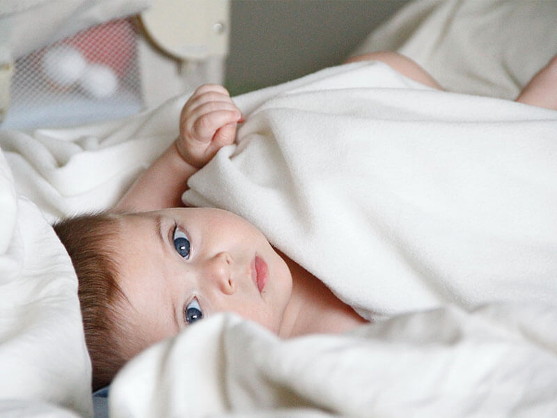 Baby schaut aus weißer Decke heraus